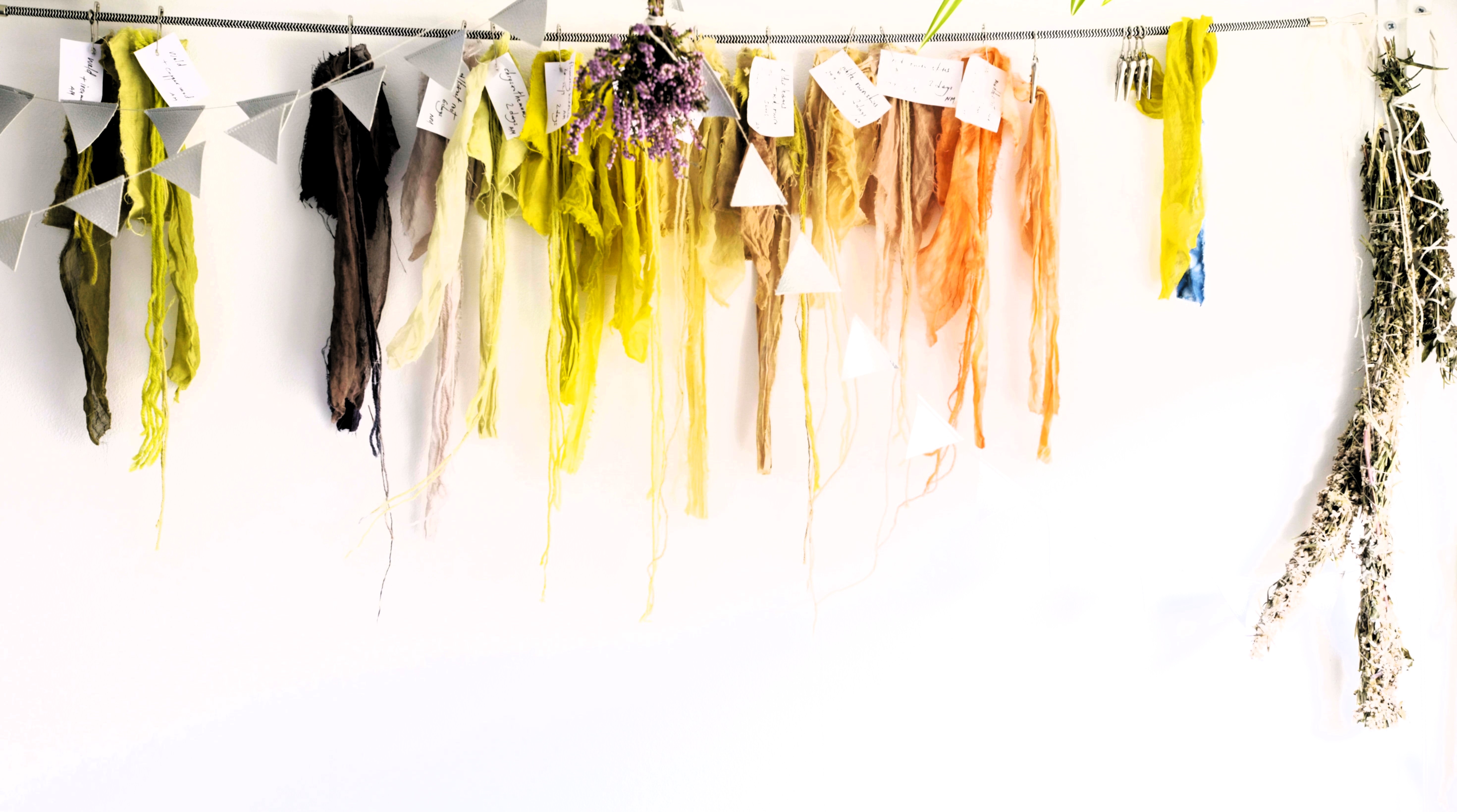 Art installation with colorful hanging fabrics, paper bunting, flowers, and dried herbs